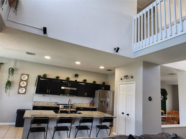 kitchen featuring a kitchen bar, light stone counters, stainless steel appliances, a kitchen island with sink, and sink