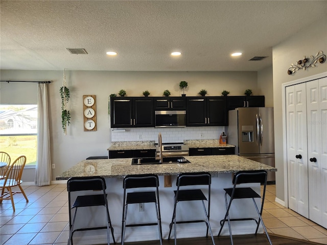 kitchen with a kitchen breakfast bar, sink, a textured ceiling, an island with sink, and appliances with stainless steel finishes