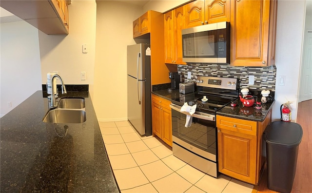 kitchen featuring decorative backsplash, stainless steel appliances, sink, light tile patterned floors, and dark stone countertops