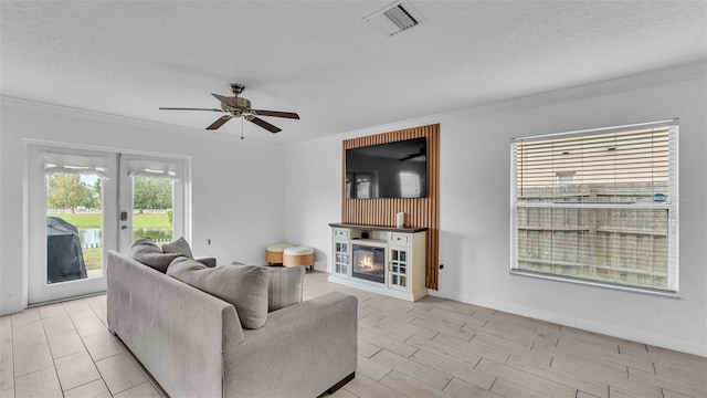 living room featuring ceiling fan, light hardwood / wood-style floors, crown molding, and a textured ceiling