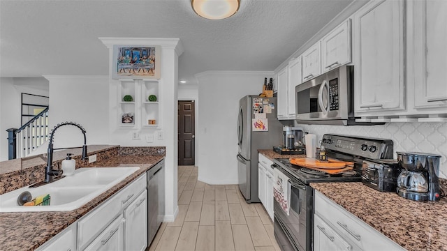 kitchen with sink, dark stone countertops, appliances with stainless steel finishes, white cabinets, and ornamental molding