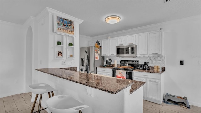 kitchen featuring dark stone counters, kitchen peninsula, appliances with stainless steel finishes, a kitchen bar, and white cabinetry