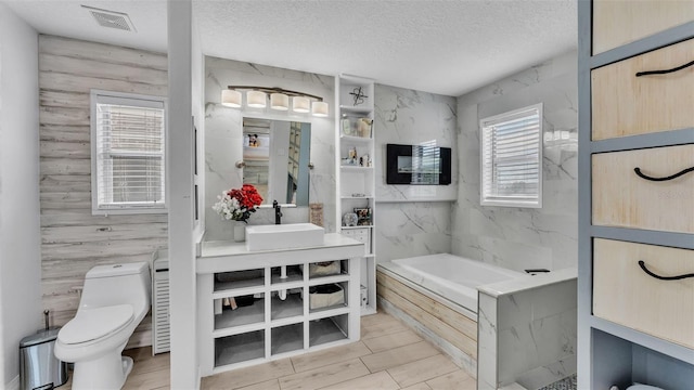 bathroom with a washtub, vanity, a textured ceiling, tile walls, and toilet