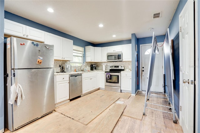 kitchen featuring light wood-type flooring, white cabinetry, backsplash, and appliances with stainless steel finishes