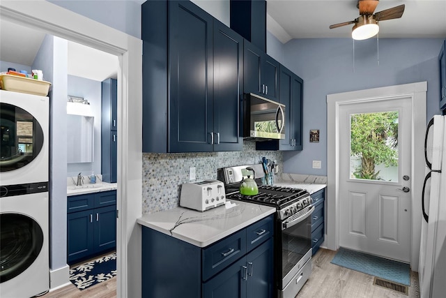 kitchen featuring lofted ceiling, stacked washer and dryer, blue cabinetry, appliances with stainless steel finishes, and light hardwood / wood-style floors