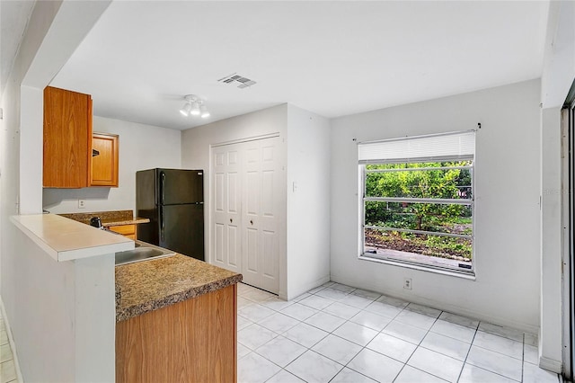 kitchen with light tile patterned floors, kitchen peninsula, black refrigerator, and sink