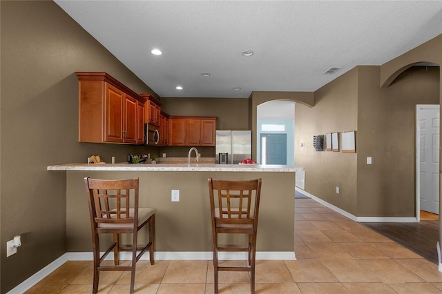 kitchen featuring light tile patterned flooring, appliances with stainless steel finishes, a kitchen breakfast bar, and kitchen peninsula