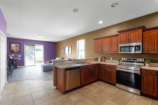 kitchen with appliances with stainless steel finishes, sink, light stone counters, kitchen peninsula, and a textured ceiling