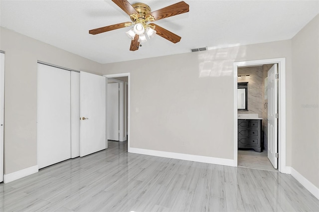 unfurnished bedroom featuring ensuite bath, a closet, ceiling fan, and light wood-type flooring