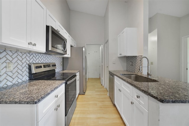 kitchen with dark stone counters, a sink, light wood-style floors, appliances with stainless steel finishes, and white cabinetry