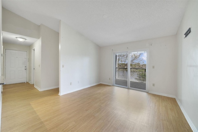 empty room featuring light wood-style flooring, a textured ceiling, baseboards, and lofted ceiling