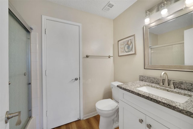 bathroom with vanity, wood finished floors, visible vents, toilet, and a shower with door