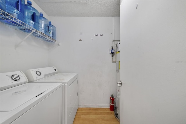 clothes washing area with a textured ceiling, laundry area, light wood-type flooring, and washer and clothes dryer