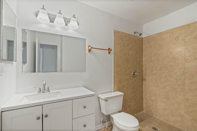 bathroom featuring a tile shower, vanity, and toilet