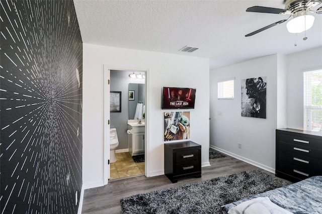 bedroom with a textured ceiling, connected bathroom, dark hardwood / wood-style floors, and ceiling fan