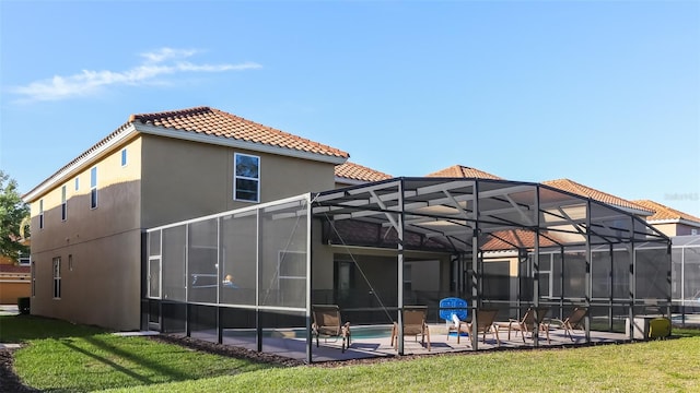 back of property with a yard, glass enclosure, and a patio area