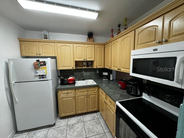 kitchen featuring decorative backsplash, light brown cabinetry, white appliances, sink, and light tile patterned flooring