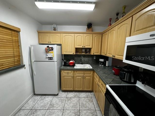 kitchen featuring light brown cabinets, white appliances, backsplash, and sink