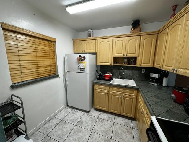 kitchen with black electric range oven, white refrigerator, sink, light tile patterned floors, and tasteful backsplash