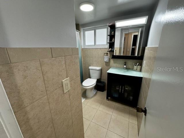 bathroom featuring tile patterned flooring, vanity, toilet, and tile walls