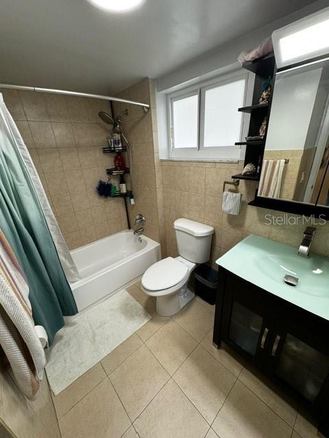 full bathroom with vanity, shower / bath combo with shower curtain, tile walls, tile patterned flooring, and toilet