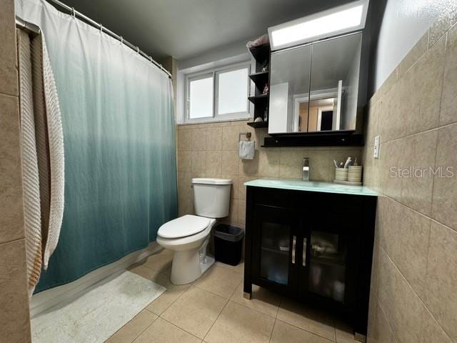 bathroom featuring tile patterned floors, vanity, tile walls, toilet, and curtained shower