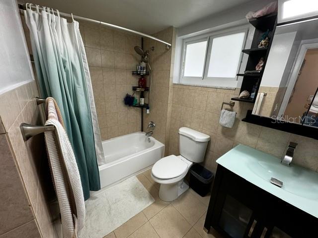 full bathroom with tile patterned floors, toilet, shower / tub combo with curtain, vanity, and tile walls