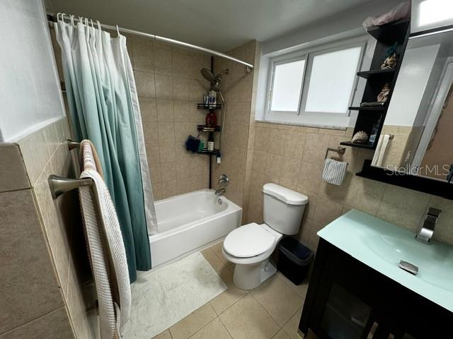 full bathroom featuring tile patterned floors, toilet, shower / bath combo with shower curtain, vanity, and tile walls