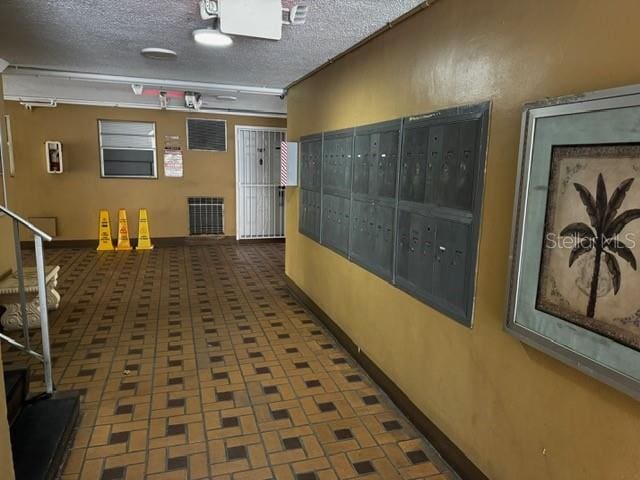 hall featuring a textured ceiling, visible vents, brick floor, and mail area