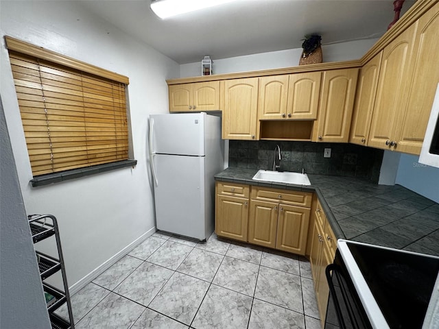 kitchen with tile counters, range, freestanding refrigerator, a sink, and backsplash