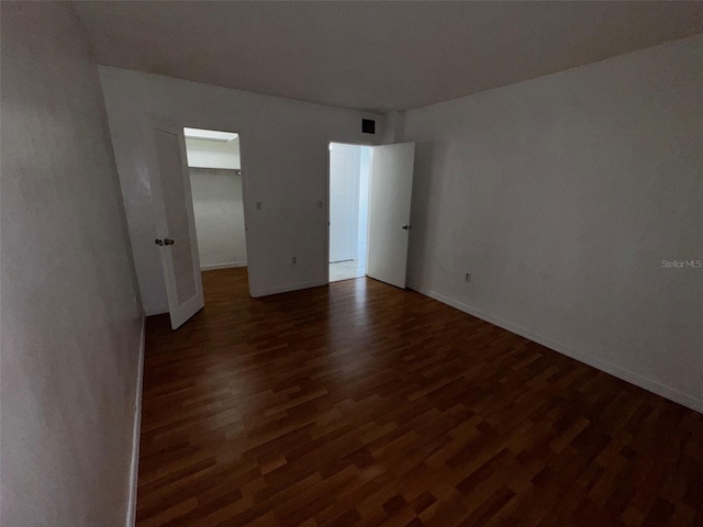 unfurnished bedroom featuring a spacious closet, baseboards, and wood finished floors