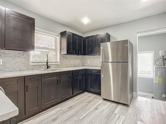 kitchen featuring sink, electric water heater, light hardwood / wood-style flooring, backsplash, and stainless steel fridge