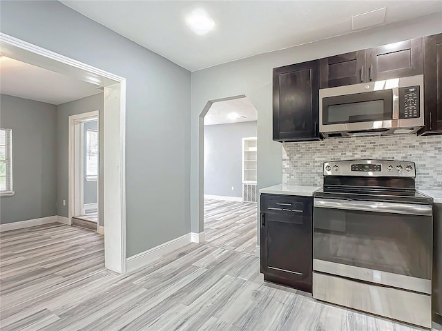 kitchen with decorative backsplash, appliances with stainless steel finishes, light hardwood / wood-style flooring, and dark brown cabinets