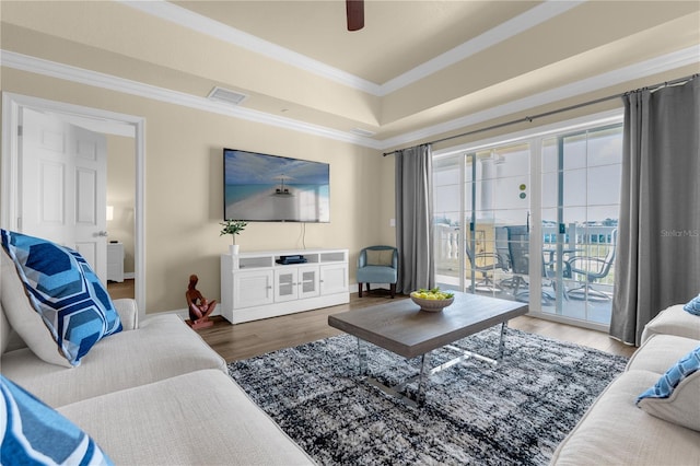 living room featuring ornamental molding, a raised ceiling, ceiling fan, and dark wood-type flooring