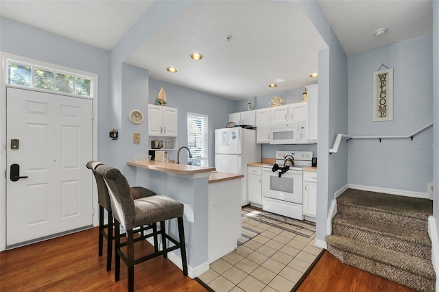 kitchen with a kitchen bar, white cabinetry, light hardwood / wood-style flooring, kitchen peninsula, and white appliances