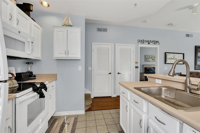 kitchen with light tile patterned floors, white appliances, white cabinetry, and sink