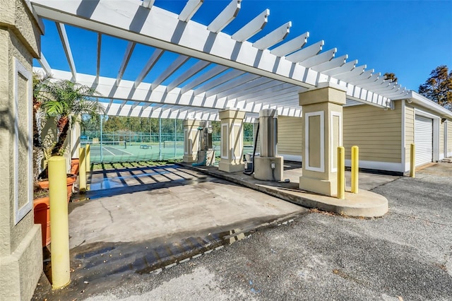 view of patio featuring a garage, tennis court, and a pergola