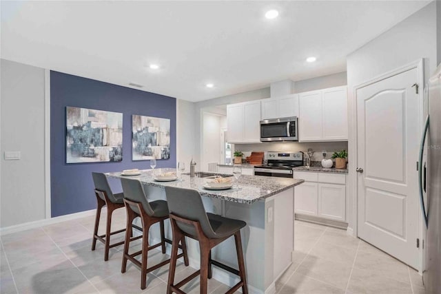 kitchen with light stone countertops, a breakfast bar, white cabinets, a center island with sink, and appliances with stainless steel finishes