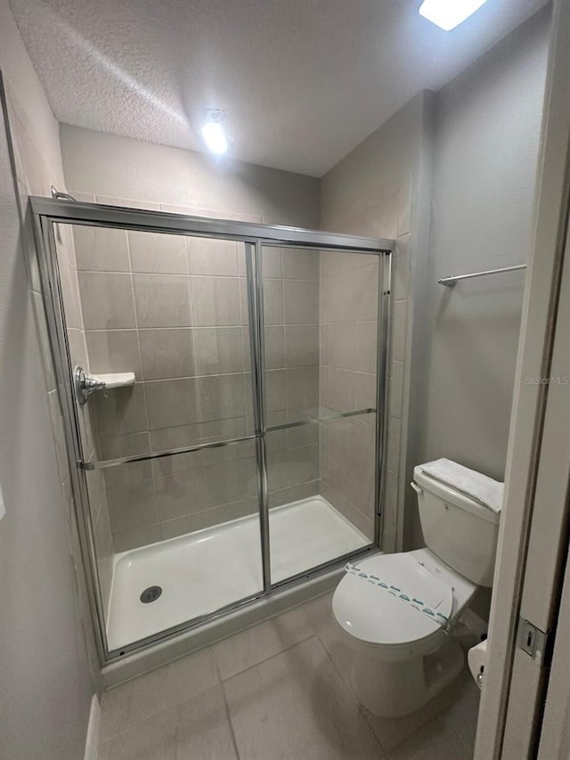 bathroom with a textured ceiling, tile patterned flooring, an enclosed shower, and toilet