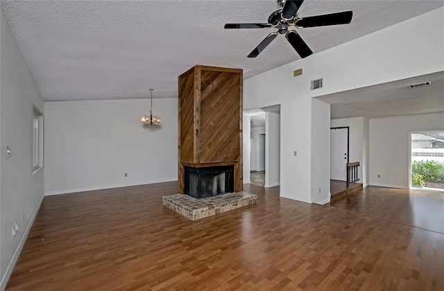 unfurnished living room with a textured ceiling, ceiling fan with notable chandelier, dark wood-type flooring, and a brick fireplace