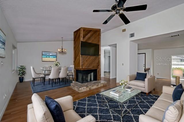 living room with ceiling fan with notable chandelier, hardwood / wood-style flooring, a brick fireplace, and vaulted ceiling