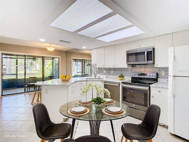 kitchen with sink, a skylight, decorative backsplash, appliances with stainless steel finishes, and white cabinetry