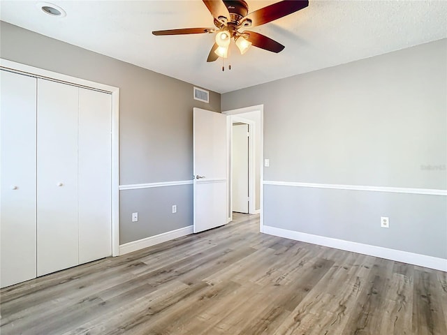 unfurnished bedroom featuring a textured ceiling, a closet, light hardwood / wood-style flooring, and ceiling fan