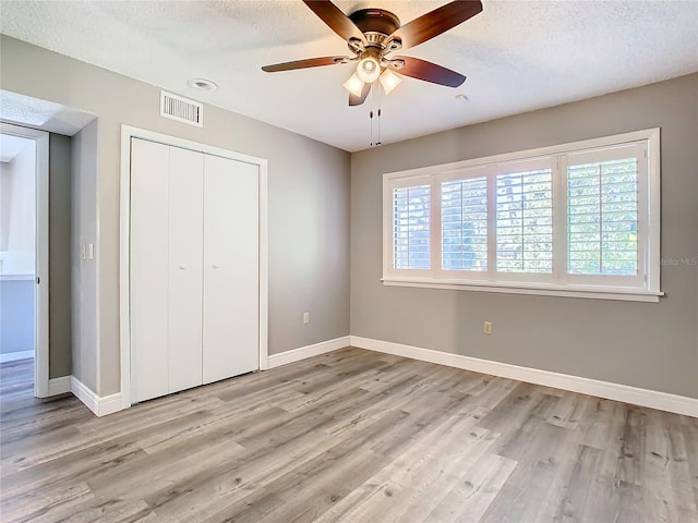 unfurnished bedroom with a textured ceiling, a closet, light hardwood / wood-style floors, and ceiling fan