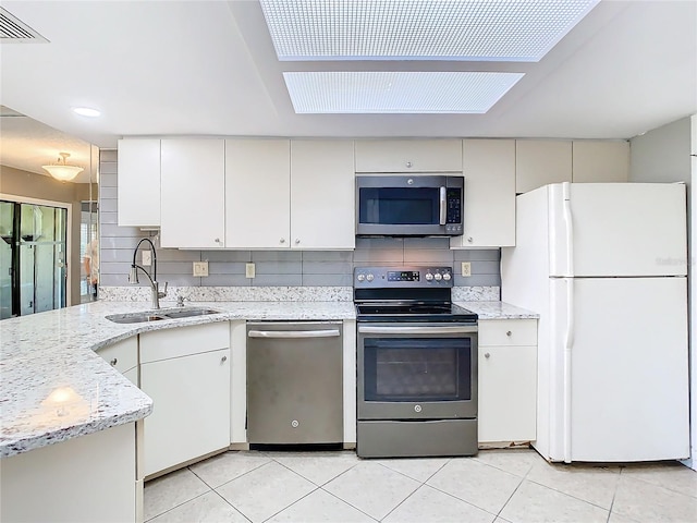 kitchen with light stone countertops, appliances with stainless steel finishes, a skylight, tasteful backsplash, and sink