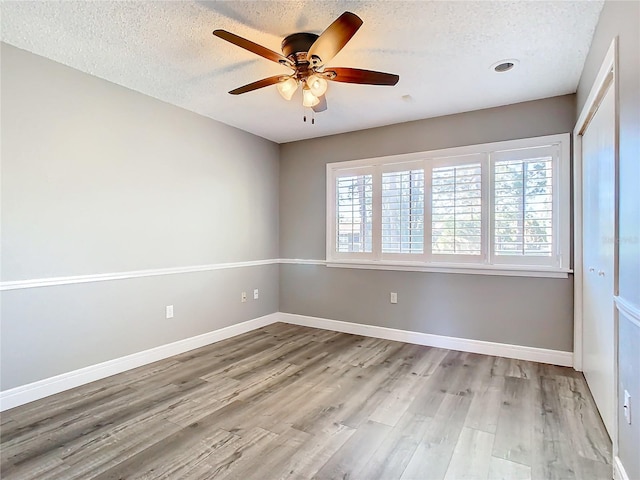 empty room with a textured ceiling, light wood-type flooring, a wealth of natural light, and ceiling fan