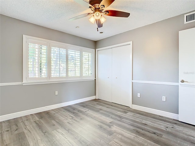 unfurnished bedroom with ceiling fan, light wood-type flooring, a textured ceiling, and a closet