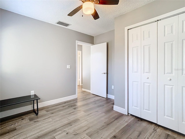 unfurnished bedroom featuring a textured ceiling, a closet, light hardwood / wood-style flooring, and ceiling fan