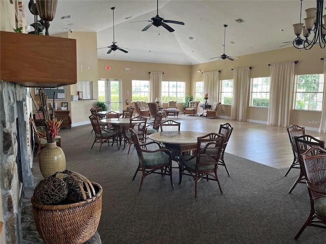 dining space featuring ceiling fan with notable chandelier, high vaulted ceiling, and dark colored carpet