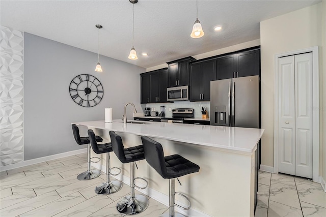 kitchen featuring a kitchen island with sink, sink, hanging light fixtures, a kitchen bar, and stainless steel appliances